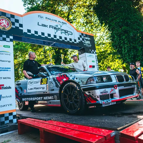 Posádka Motorsport Němec s poháry na cílové rampě Rallye Plzeň 2026, před nimi BMW M3 E36